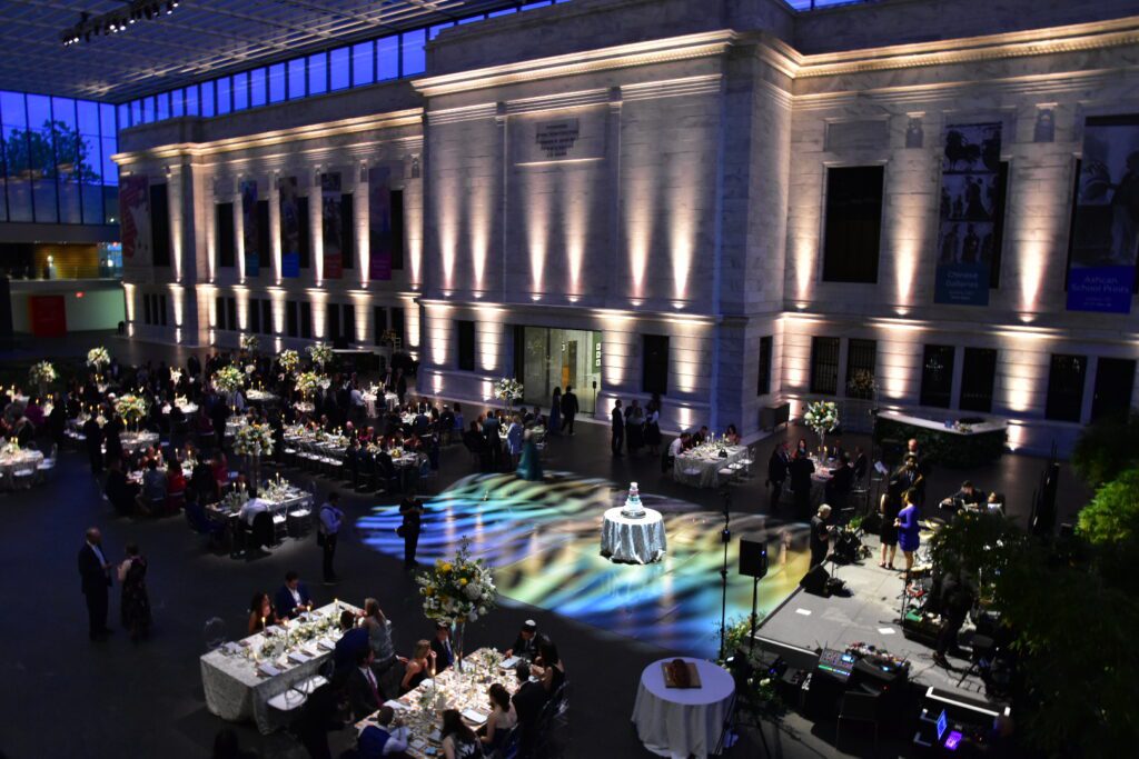 Interior event space of a stone building with white uplighting, a dance floor, and tables.