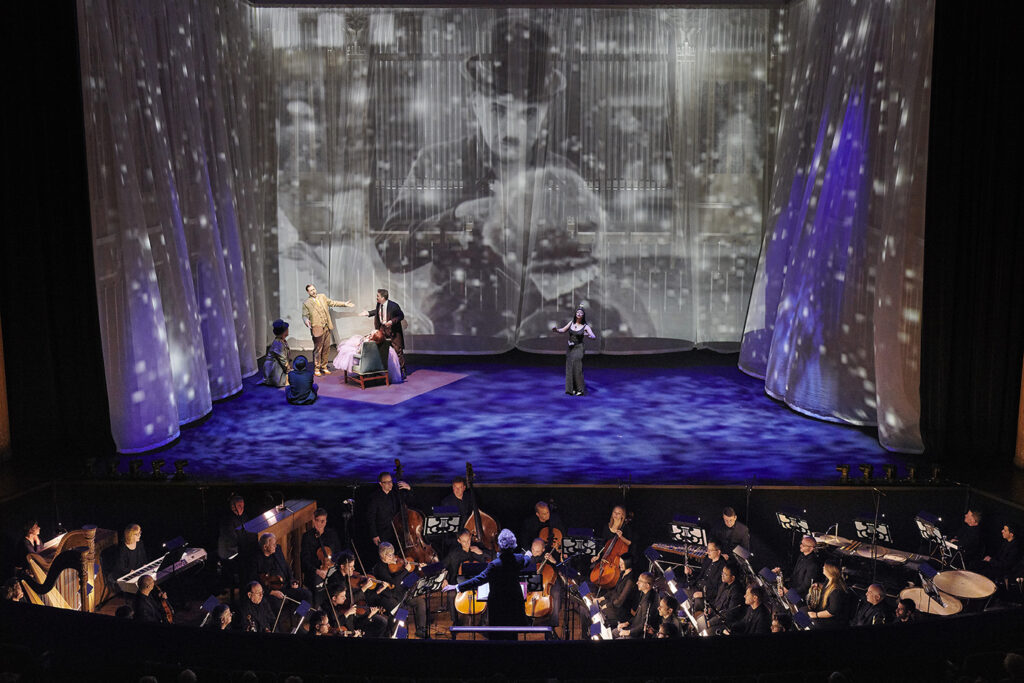 A performance stage featuring an orchestra in the front and a projection of Charlie Chaplin on a white curtain in the back.