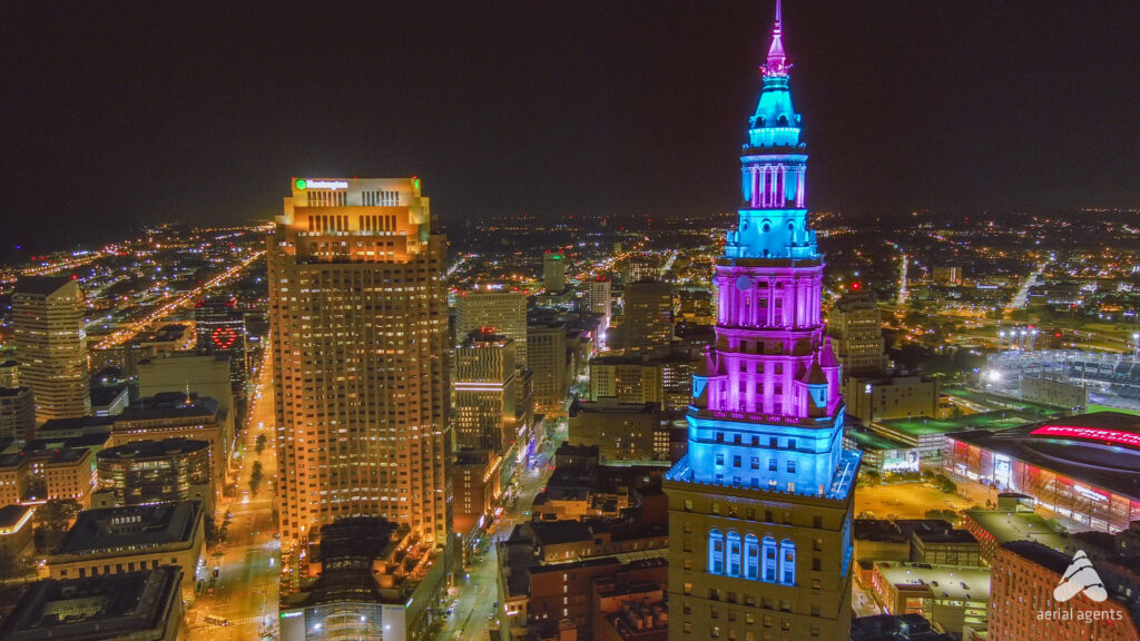 The top of a building lit up with blue and purple lights overlooking a city at night.