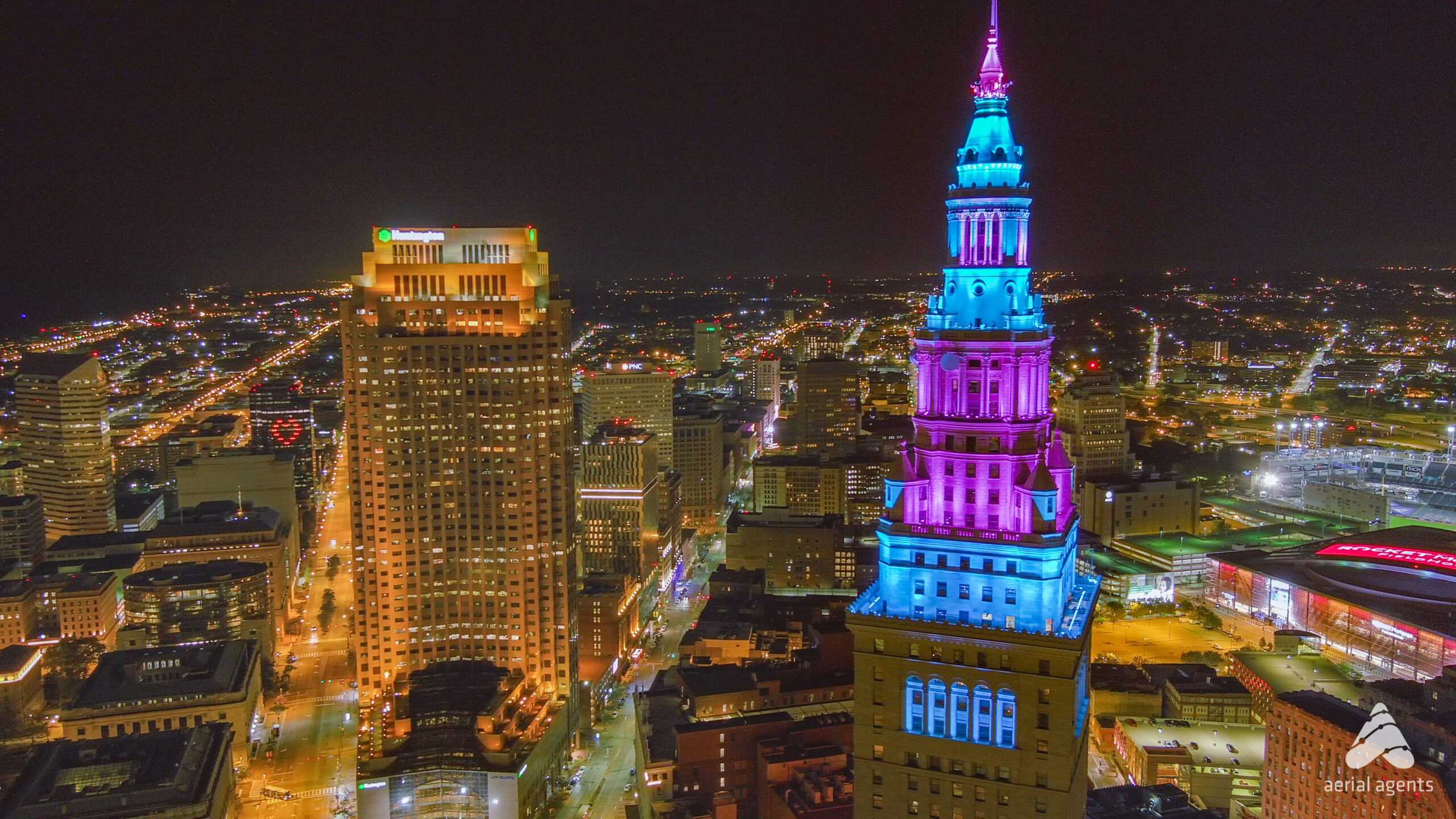 The top of a building lit up with blue and purple lights overlooking a city at night.